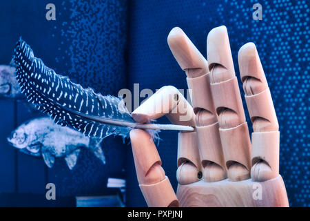 Artikuliert Holz- hand zart Holding eine Feder auf einem blauen Hintergrund mit Fisch Stockfoto