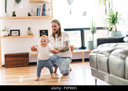 Vater helfen Baby Tochter nehmen die ersten Schritte zu Hause Stockfoto