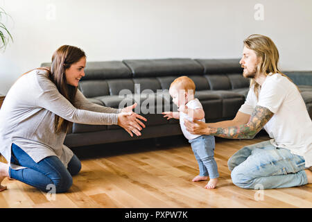 Eltern helfen Baby Tochter nehmen die ersten Schritte zu Hause Stockfoto