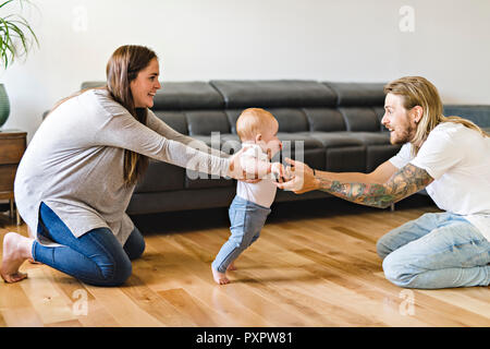 Eltern helfen Baby Tochter nehmen die ersten Schritte zu Hause Stockfoto