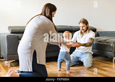 Eltern helfen Baby Tochter nehmen die ersten Schritte zu Hause Stockfoto