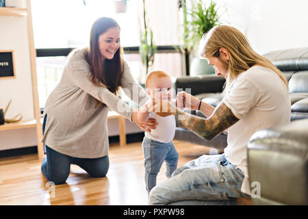 Eltern helfen Baby Tochter nehmen die ersten Schritte zu Hause Stockfoto