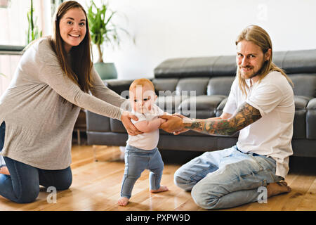 Eltern helfen Baby Tochter nehmen die ersten Schritte zu Hause Stockfoto