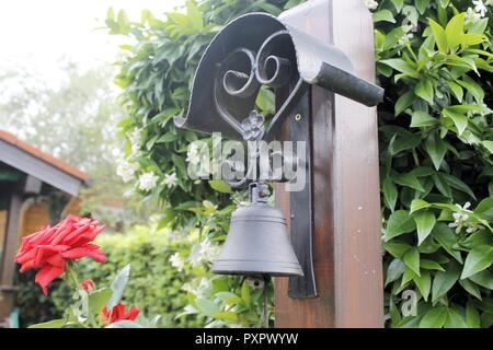 Kleine Glocke in einem Garten unter Blätter und Blumen Stockfoto