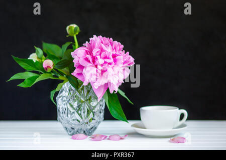 Tasse Tee und Pfingstrosen in einer Vase auf dem Tisch. Schwarzen Hintergrund. Stockfoto