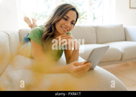 Lächelnd reife Frau liegen auf der Couch zu Hause mit der Tablette Stockfoto