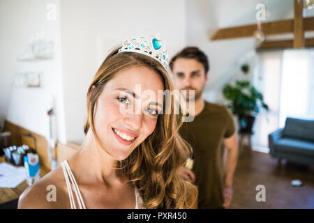 Porträt der lächelnde Frau tiara zu Hause tragen mit Mann im Hintergrund Stockfoto