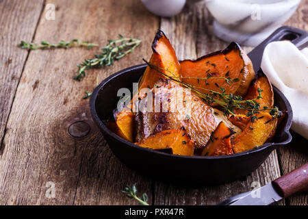 Hähnchen Schenkel mit in Scheiben geschnittenen Kürbis Kürbis und frischem Thymian in Gusseisen Skillet auf rustikalen Holztisch, Herbst oder Winter gemütliche Abendessen Stockfoto