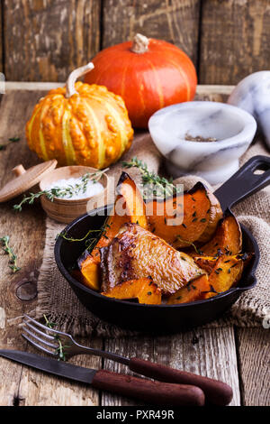 Hähnchen Schenkel mit in Scheiben geschnittenen Kürbis Kürbis und frischem Thymian in Gusseisen Skillet auf rustikalen Holztisch, Herbst oder Winter gemütliche Abendessen Stockfoto