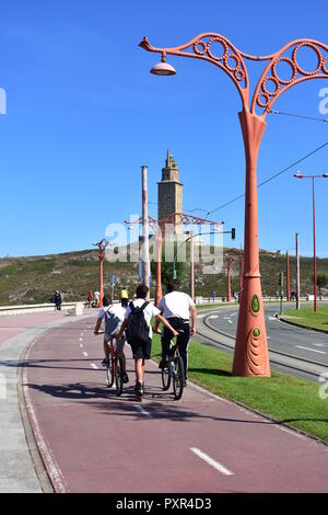 Junge Leute Schlittschuhlaufen und Radfahren in einer Promenade mit Straßenbahnschienen und Denkmal. Torre de Hercules Park, A Coruña, Galicien, Spanien. Stockfoto