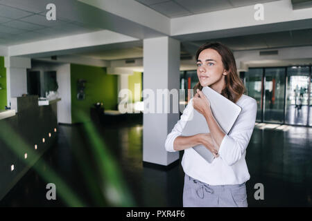 Geschäftsfrau, die sich in Büro-, Holding Laptop Stockfoto