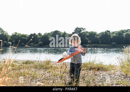 Junge spielt mit einem Spielzeug Flugzeug am Flußufer Stockfoto