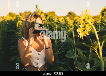 Junge Frau in einem Feld mit Sonnenblumen Bilder aufnehmen mit einem Instant Kamera Stockfoto
