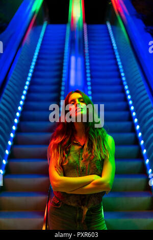 Portrait von beleuchteten junge Frau vor der blau beleuchtete Rolltreppe Stockfoto