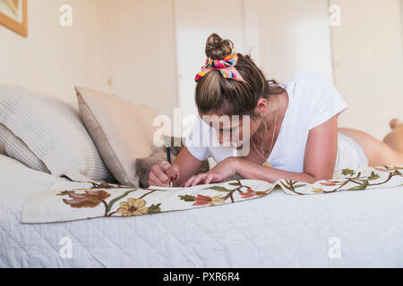 Junge Frau liegend auf Bett zu Hause schreiben in Tagebuch Stockfoto