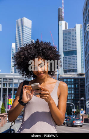 Deutschland, Frankfurt, Portrait von lächelnden jungen Frau mit lockigem Haar mit Handy Stockfoto