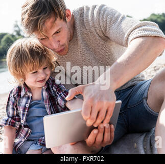 Vater und Sohn spielen auf digital Tablet am Flußufer Stockfoto