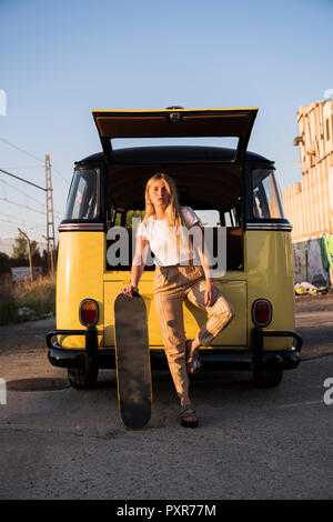 Junge Frau mit außerhalb Skateboard stehend an einem Jahrgang van Stockfoto