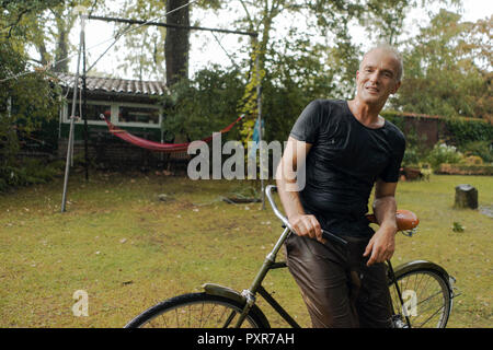 Portrait von reifer Mann mit Fahrrad im Sommer Regen im Garten Stockfoto