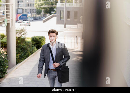 Lächelnd Geschäftsmann mit Crossbody-tasche in der Stadt in Bewegung Stockfoto