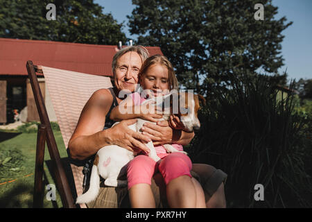 Lächelnd Oma mit Enkelin und Hund auf dem Liegestuhl im Garten Stockfoto