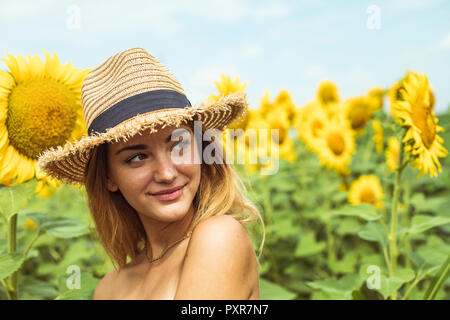 Junge Frau mit einem Strohhut lächelnd in einem Feld mit Sonnenblumen Stockfoto