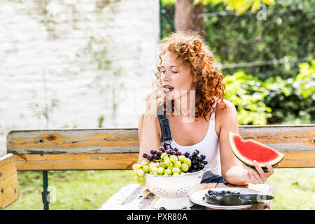 Rothaarige junge Frau Trauben essen im Sommer Stockfoto