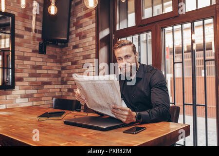 Portrait einer jungen Bartgeier Geschäftsmann am Tisch sitzen und Zeitung lesen. Stockfoto
