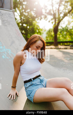 Rothaarige Frau sitzt in einem Skatepark durch Sonnenuntergang Stockfoto