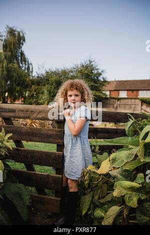 Portrait von kleinen Mädchen öffnen Tor im Garten Stockfoto