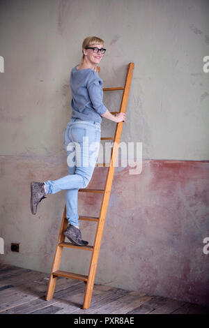 Lächelnde Frau stehend auf die Leiter in einem unrenovierten Zimmer eines Loft Stockfoto