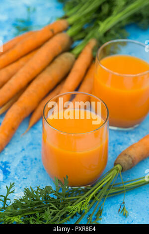 Zwei Gläser mit frischem Karottensaft und Karotten auf hellblauem Grund Stockfoto