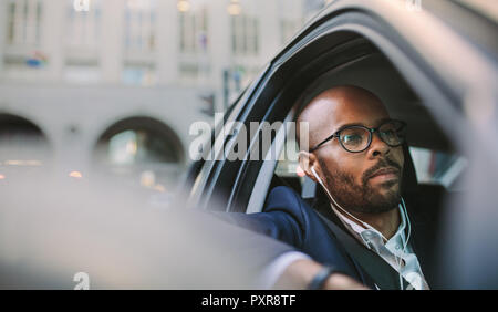 Geschäftsmann, tragen, Kopfhörer und Zuhören, dazu während der Fahrt ein Auto. Afrikanischen Geschäftsmann in morgen Stau. Stockfoto