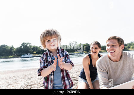 Happy Boy händeklatschen am Flußufer mit Eltern Stockfoto