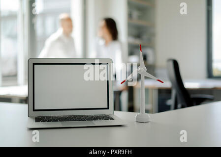 Laptop und Modell des Windrad im Regal im Büro, mit zwei Personen im Gespräch in Hintergrund Stockfoto