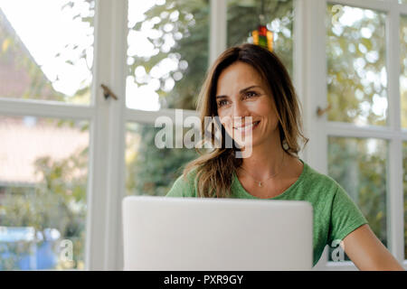 Lächelnd reife Frau am Fenster mit Laptop Stockfoto