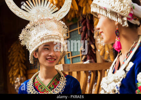 China, Yunnan, zwei lächelnde junge Miao Frauen in traditionellen Gewändern und Kopfbedeckungen Stockfoto