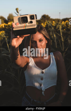 Junge Frau in einem Feld mit Sonnenblumen mit einem Instant Kamera Stockfoto