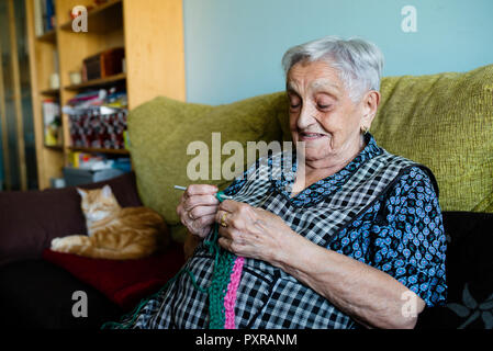 Porträt von senior Frau sitzt auf der Couch neben ihrem schlafenden Katzen häkeln Stockfoto