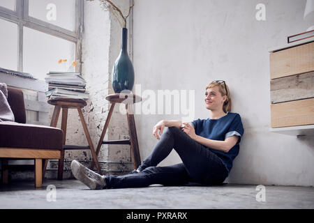 Lächelnde Frau auf dem Boden sitzend auf dem Dachboden Stockfoto