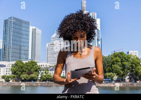 Deutschland, Frankfurt, lächelnden jungen Frau mit lockigem Haar mit Tablet in der Stadt Stockfoto