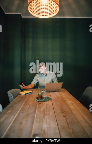 Man sitzt im Büro, zu spät in seinem Start-up-Unternehmen, mit Laptop und Smartphone Stockfoto