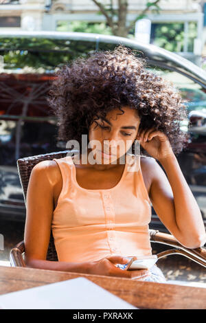 Porträt der jungen Frau mit dem lockigen Haar im Straßencafé in der Zelle Telefon sitzen Stockfoto