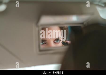 Frau gespiegelt im Rückspiegel mascara Anwendung im Auto. Stockfoto