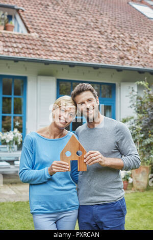 Portrait von lächelnden Paar steht vor ihrem Haus holding Haus Modell Stockfoto