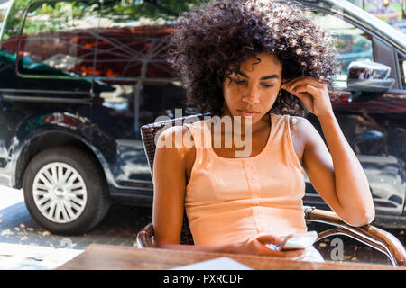 Porträt der jungen Frau mit dem lockigen Haar im Straßencafé in der Zelle Telefon sitzen Stockfoto