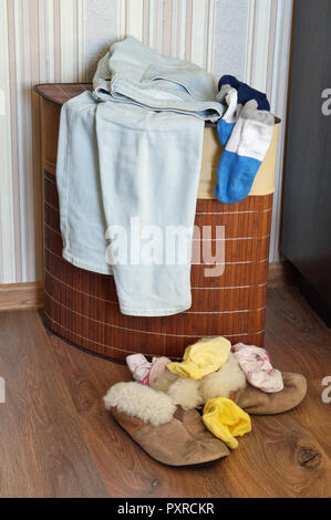 Das alte Fell Frauen Haus Hausschuhe und Socken liegen ein Haufen auf dem Holzboden. In der Nähe befindet sich ein Korb mit schmutzigen Kleidung und Jeans. Chaos in der Frauen Zimmer? Stockfoto