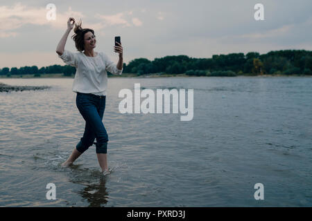 Lachende Frau am Flußufer läuft, Sie ihr Smartphone Stockfoto