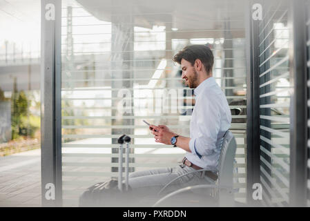 Unternehmer sitzen auf Bahnsteig mit Handy Stockfoto