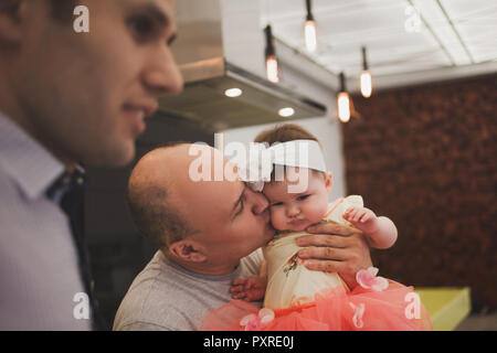 Abendessen mit der Familie. Familie empfängt Gäste, ein festliches Meeting. Opa kisses baby Enkelin Stockfoto